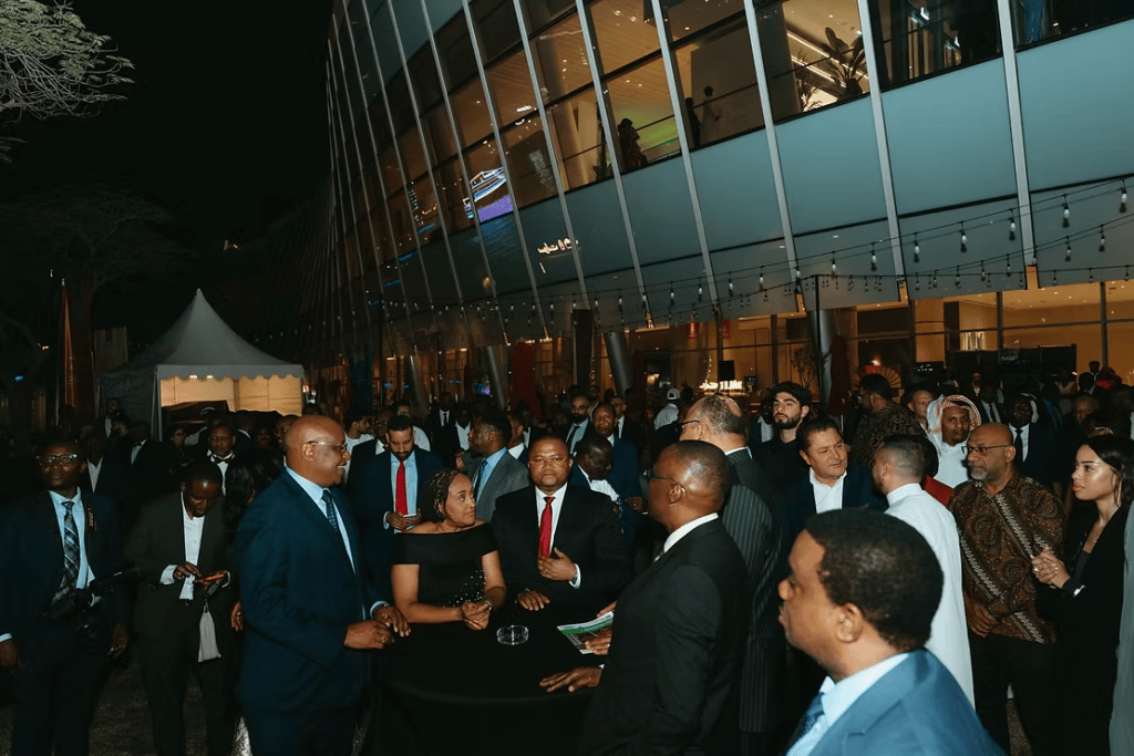 A crowd of elegantly dressed people socializing during a nighttime event outside a modern building, with a festive atmosphere and decorative lights.